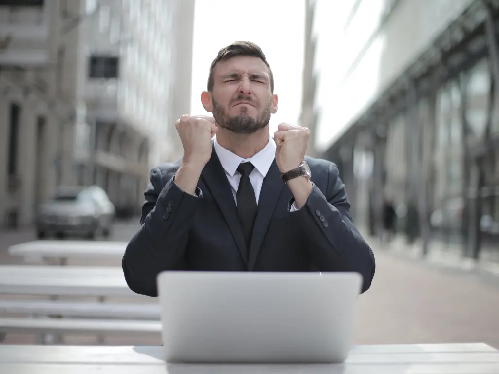 A man showing success in front of a laptop