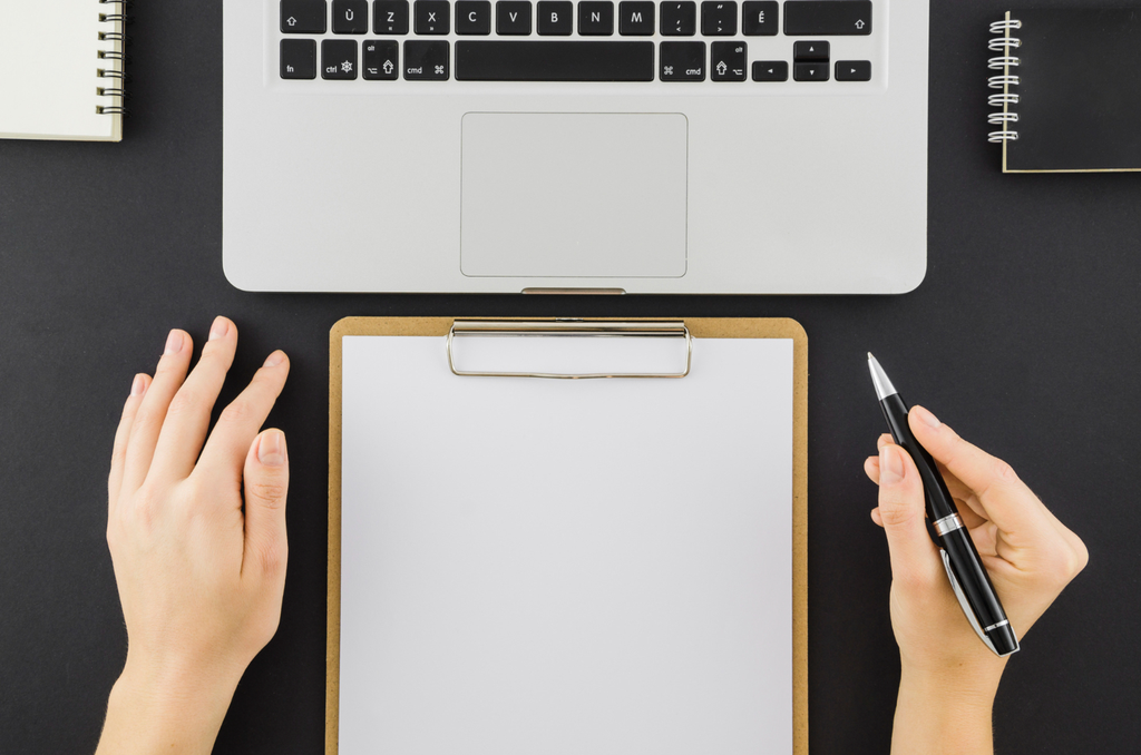 A copywriter holding a pen ready to write on his clipboard facing a laptop