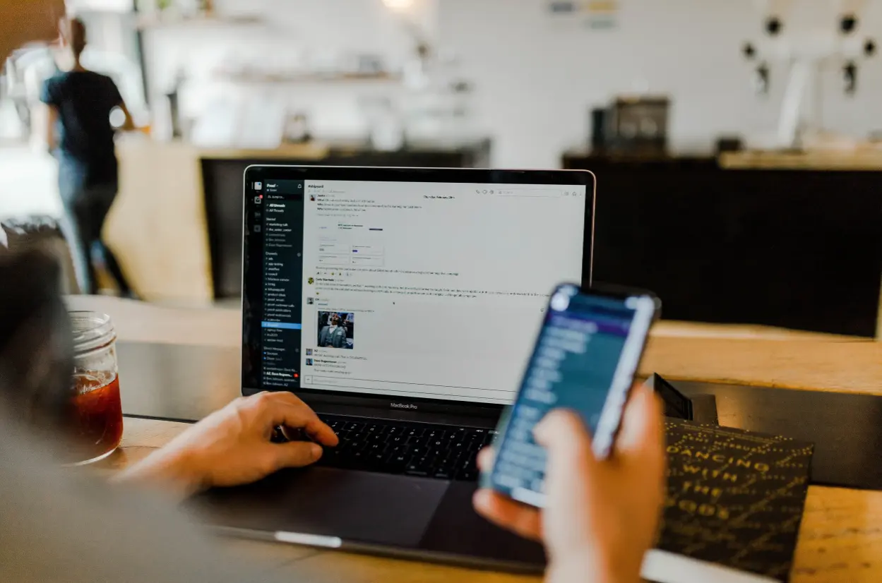 A person holding a phone while writing a message on his computer